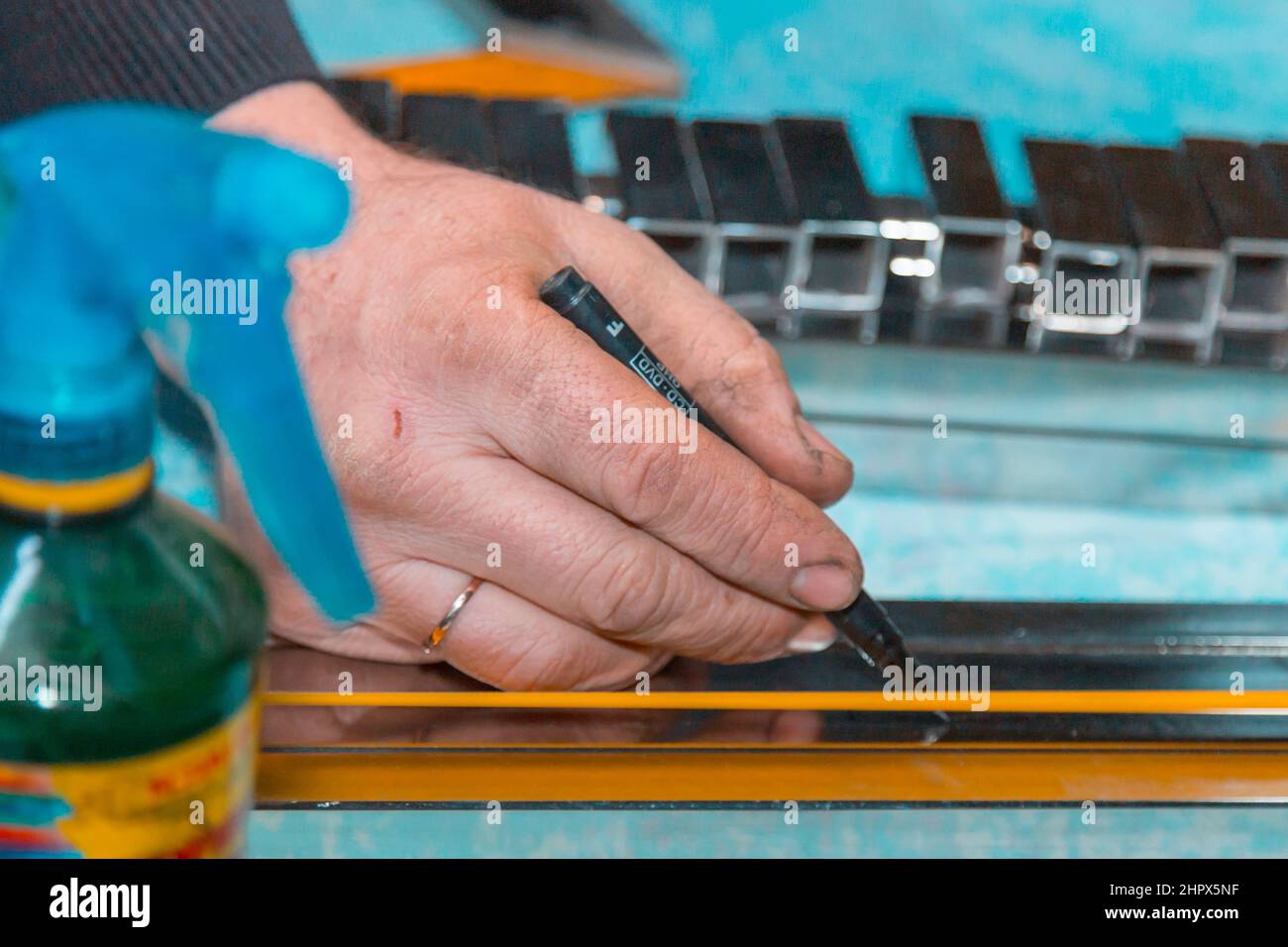 Ein Arbeiter markiert ein Edelstahlprofil mit einem Marker mit einem Maßband Stockfoto