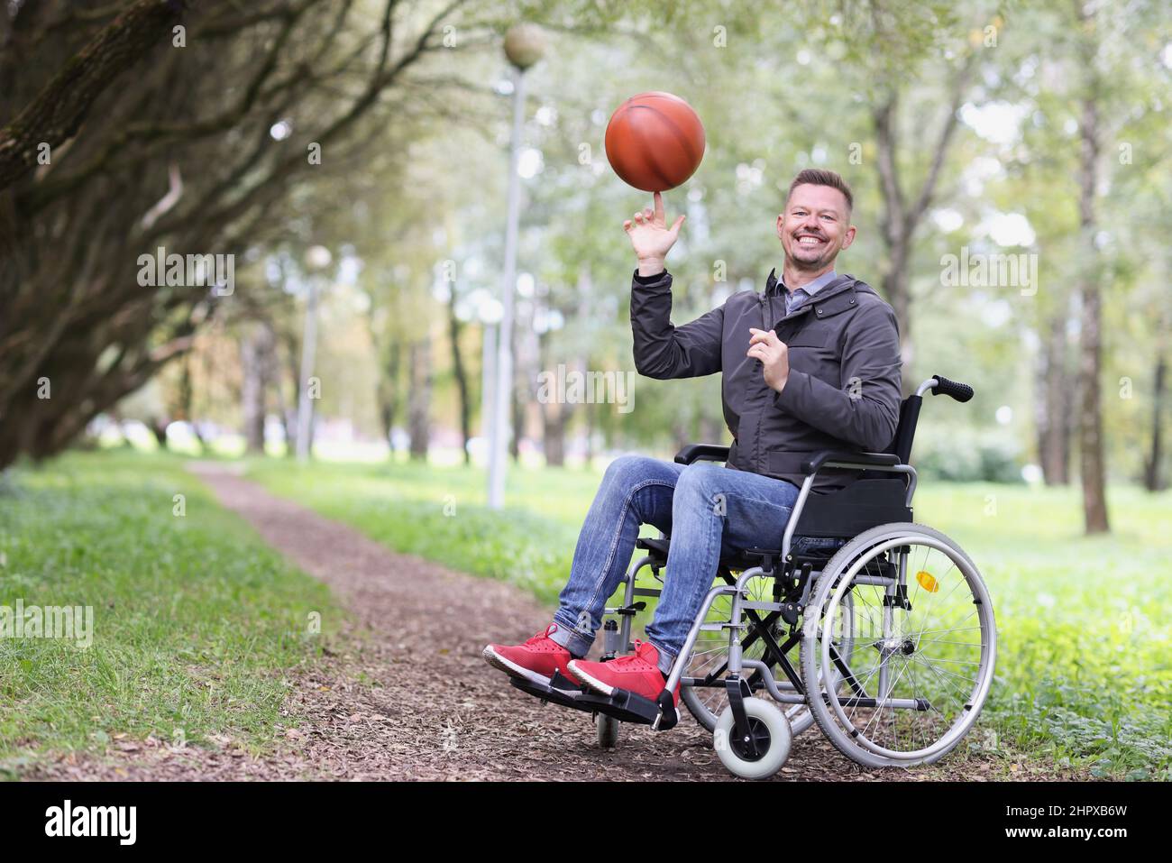 Glücklicher Mann im Rollstuhl dreht den Ball auf seinem Finger im Park Stockfoto