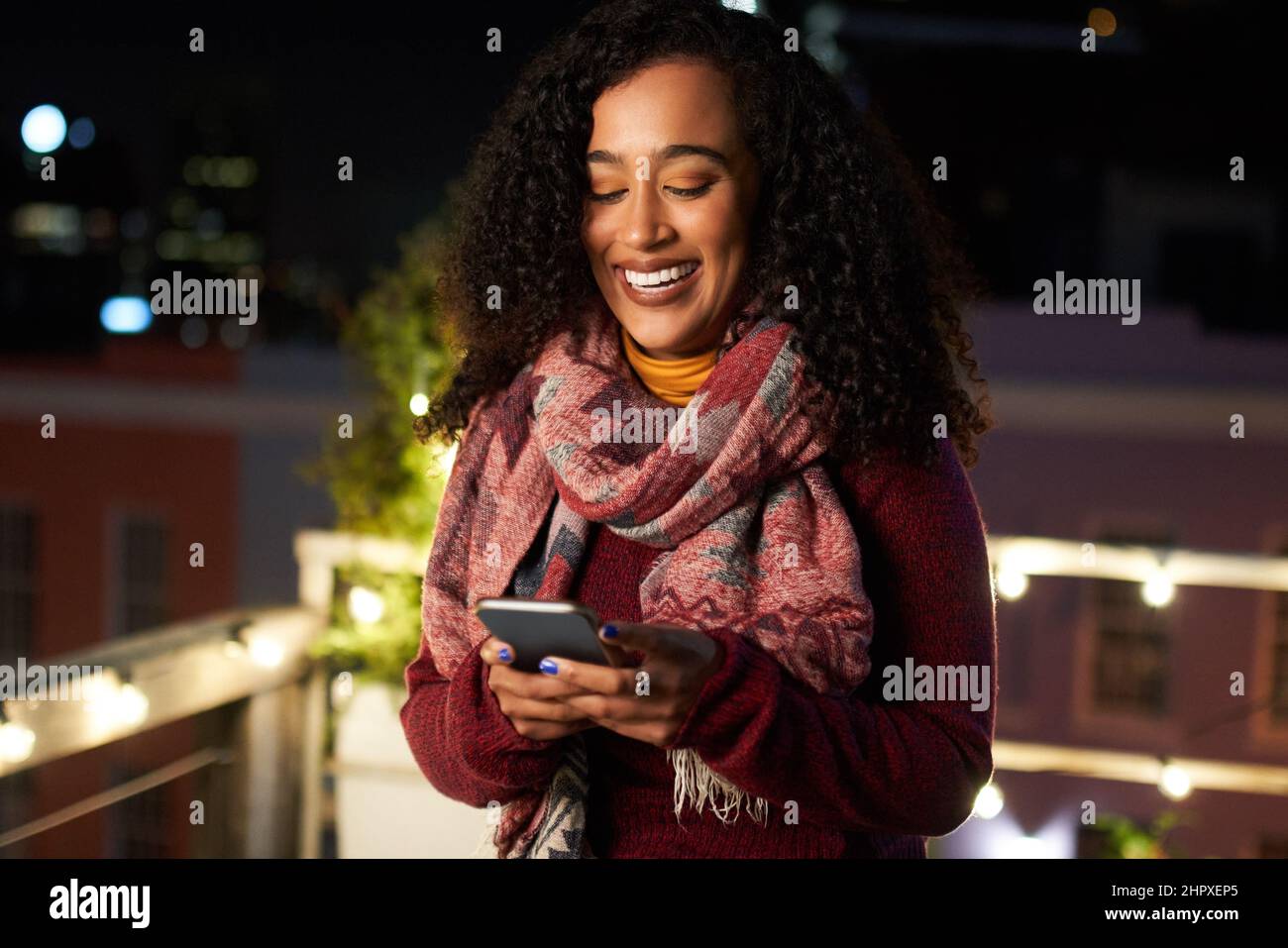 Porträt einer selbstbewussten jungen erwachsenen Frau, die auf der Dachterrasse bei einer Nachtparty auf dem Handy schreibt. Stockfoto