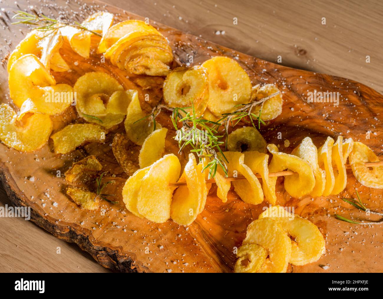 Einige frittierte, spiralförmig geschnittene Kartoffeln mit etwas Thymian auf Holzbrett Stockfoto