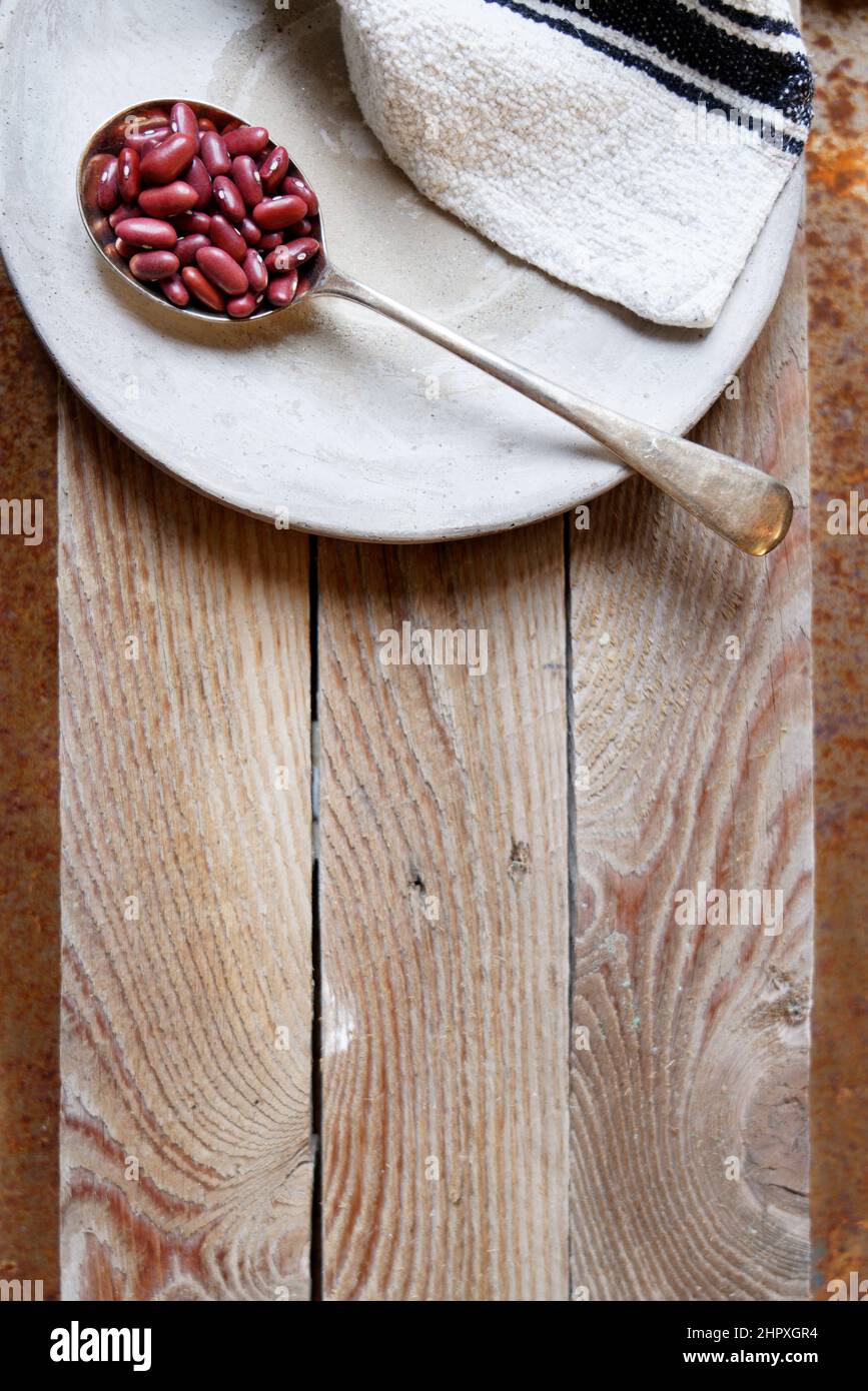 Keramikplatte mit Löffel mit Azuki-Bohnen, auf alten Holzbohlen Hintergrund, Kopierplatz, leerer Platz für Produkt, Küchenkonzept, kreatives Layout, oben Stockfoto