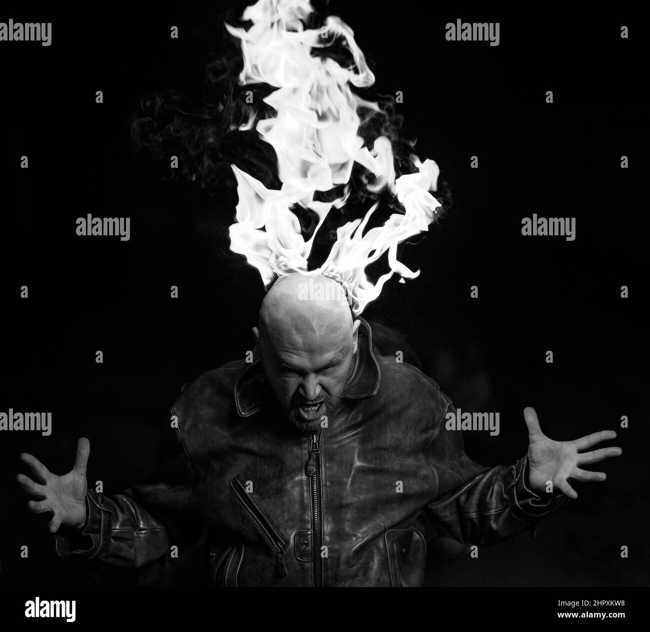 Kahlköpfiger Mann in einer Lederjacke mit brennendem Kopf auf dunklem Hintergrund. Stockfoto