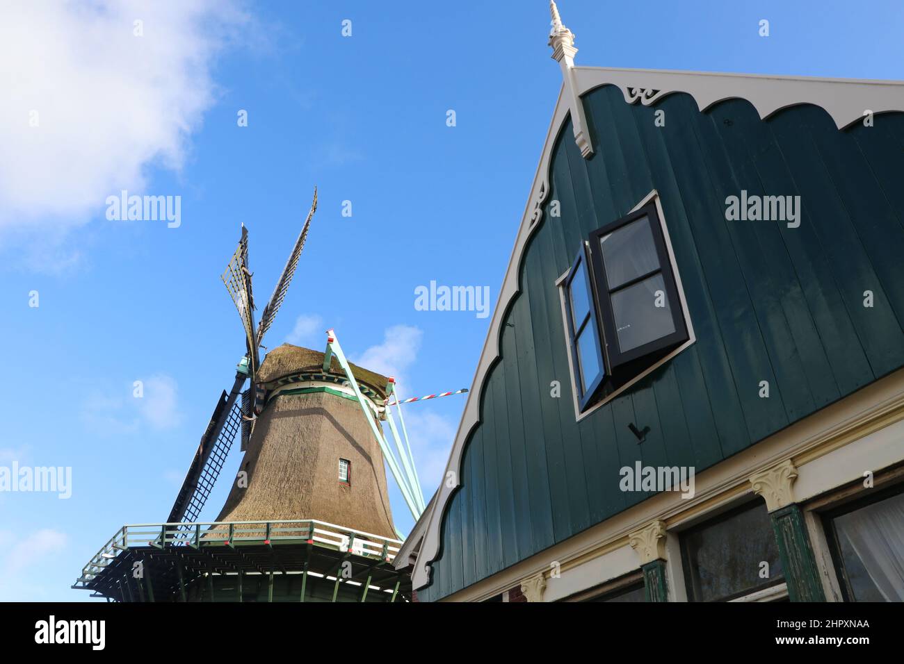 Traditionelles Holzhaus und Windmühle De Bleeke Gegen blauen Himmel mit Wolken in Zaandijk, Niederlande, Februar 2022 Stockfoto