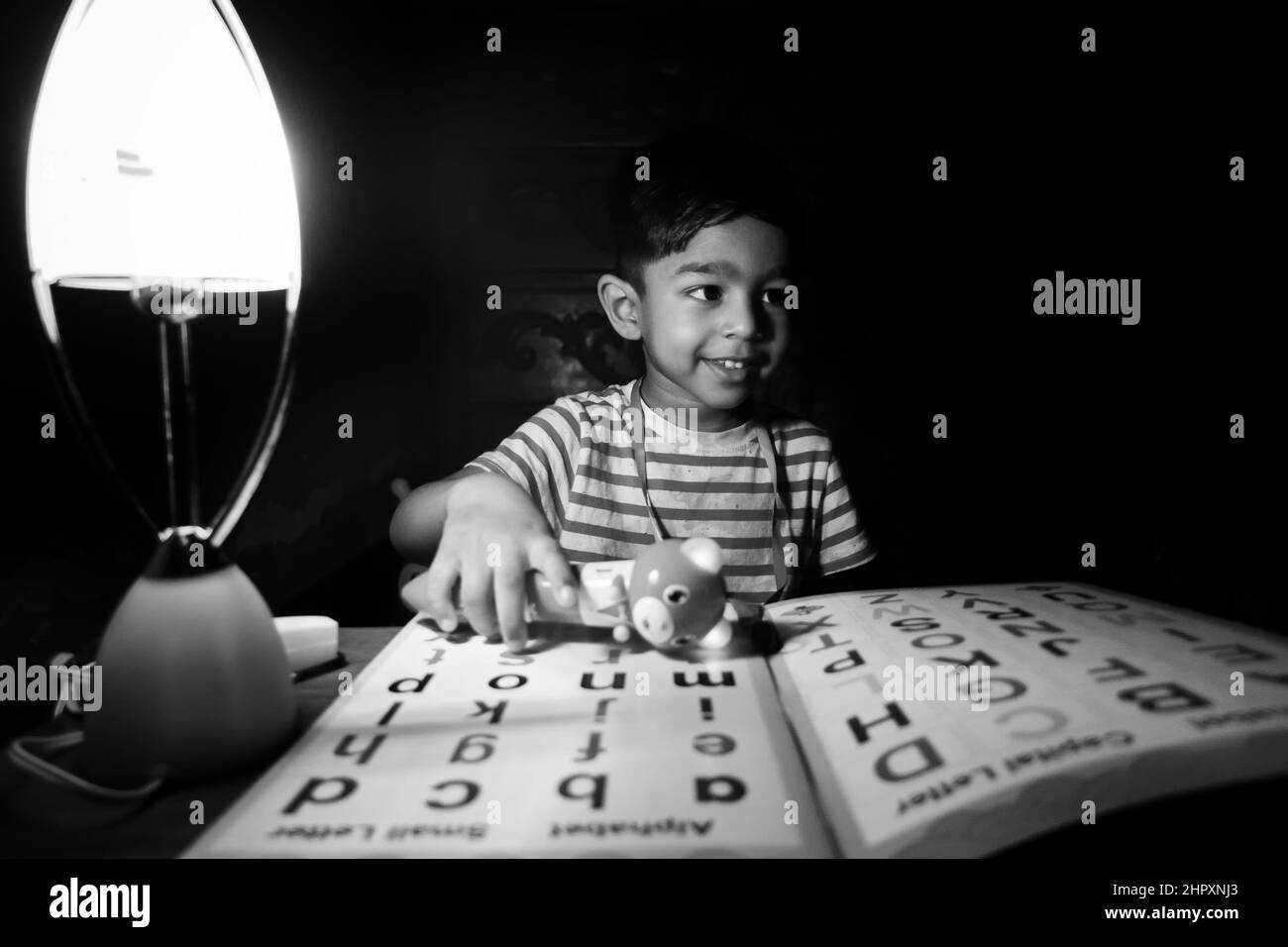 Ein Junge, der abends zu Hause mit einer Ladelampe das englische Alphabet lernt. Asiatische junge studieren unter die Lampe. Kind pädagogisches Konzept Foto. Stockfoto