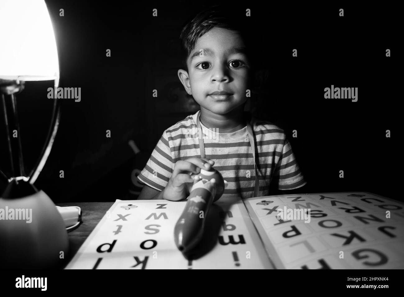 Ein Junge, der abends zu Hause mit einer Ladelampe das englische Alphabet lernt. Asiatische junge studieren unter die Lampe. Kind pädagogisches Konzept Foto. Stockfoto