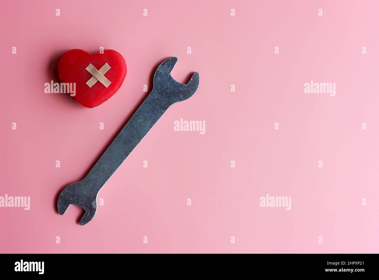 Reparieren, reparieren ein gebrochenes Herzkonzept. Rotes Herz, Verband und Schraubenschlüssel auf rosa Hintergrund mit Kopierfläche. Stockfoto