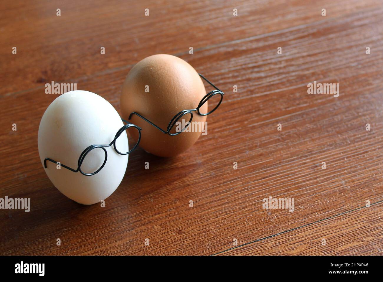 Ähnliches, aber anderes Konzept. Weißes Ei und braunes Ei tragen Gläser auf Holztisch Stockfoto