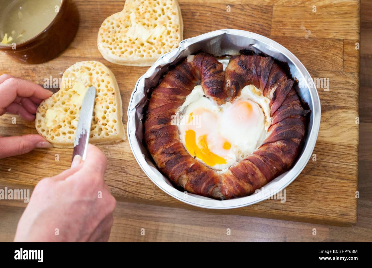 Ein skurriles Valentinstag-Frühstück mit herzförmigen Schweinen in Decken oder Wurst und Speck mit Spiegeleiern mit gebutterten Krümeln Stockfoto