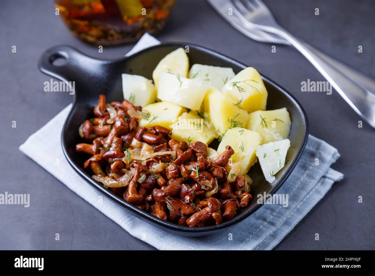 Pfifferlinge mit gekochten Kartoffeln, Zwiebeln, Dill und Öl in einer kleinen schwarzen Pfanne. Traditionelles russisches Gericht. Schwarzer Hintergrund, Nahaufnahme, Kamera-Zo Stockfoto