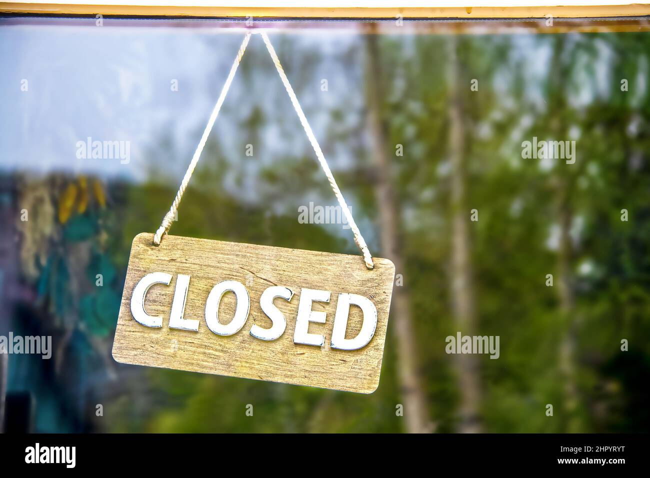 Rustikales, geschlossenes Holzschild an einem Seil, das an der Business-Glastür hängt und Kiefernwald reflektiert - Nahaufnahme und Platz für Kopien Stockfoto