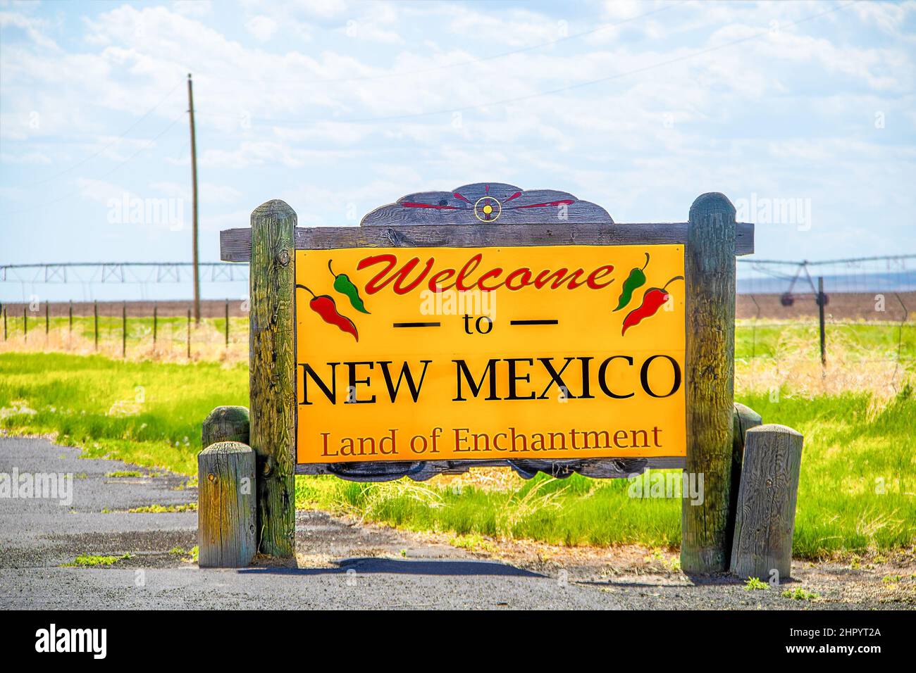Rustikales Holzschild am Straßenrand - Willkommen in New Mexico Land of Enchantment mit rollendem Bewässerungssystem im Feld hinter verschwommen Stockfoto