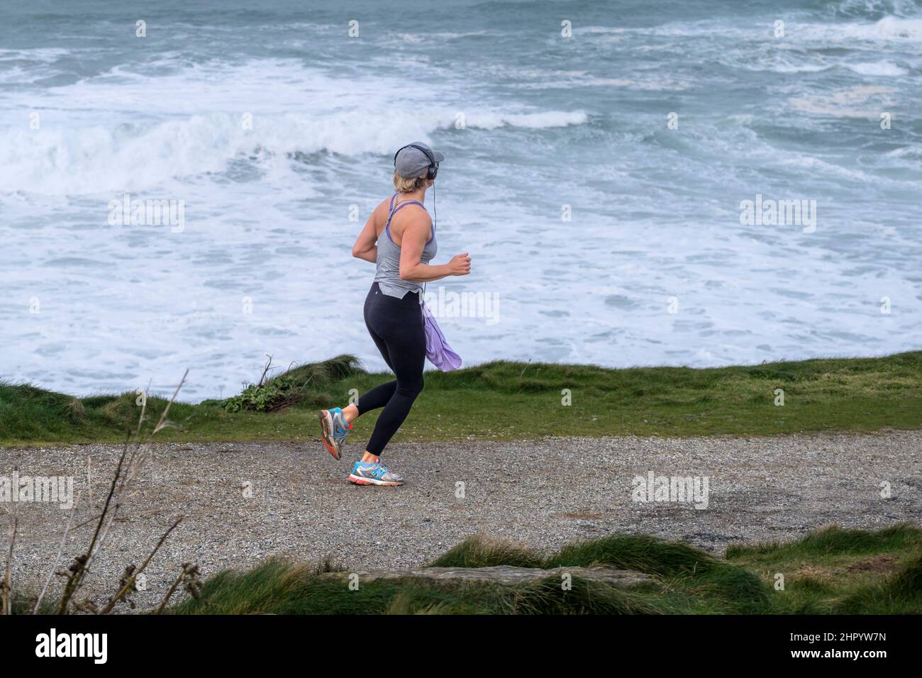 Eine Frau, die am Küstenpfad in Towan Head in Newquay in Cornwall entlang läuft. Stockfoto
