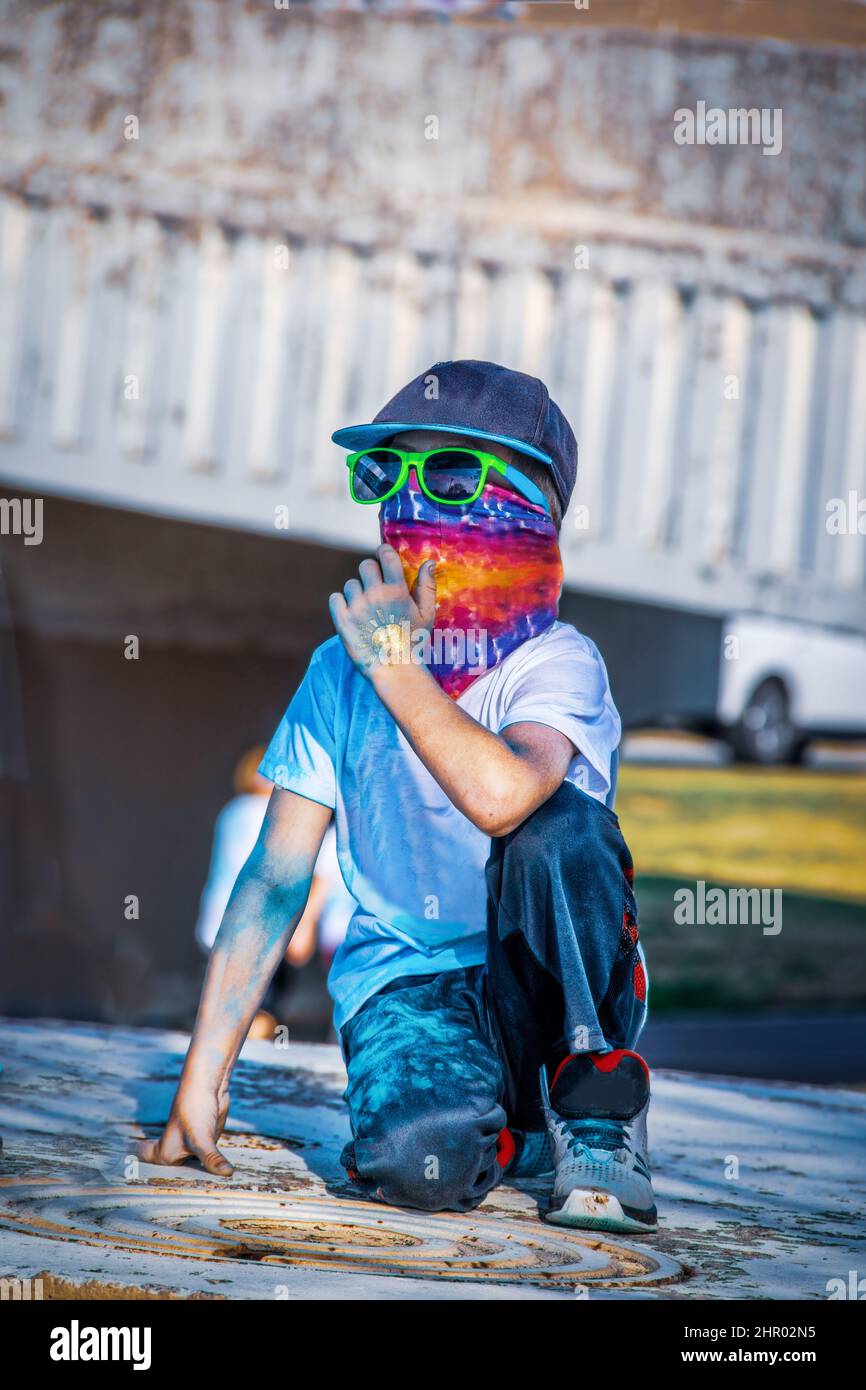 Cooles Kind, das einen Farblauf mit Bandana und Sonnenbrille und Hut beobachtet, der Gesicht und gepuderte Farbe auf Jeans und T-Shirt und Body bedeckt und temporären glitt Stockfoto