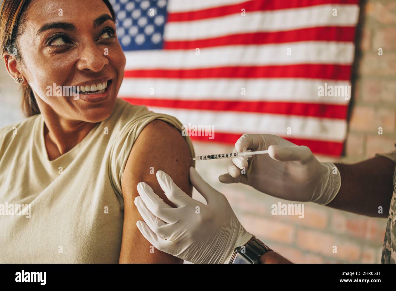 Während der Coronavirus-Pandemie wird eine US-Militärangehörige geimpft. Fröhliche Soldatin, die fröhlich lächelt, während sie die Covid-19 va erhält Stockfoto