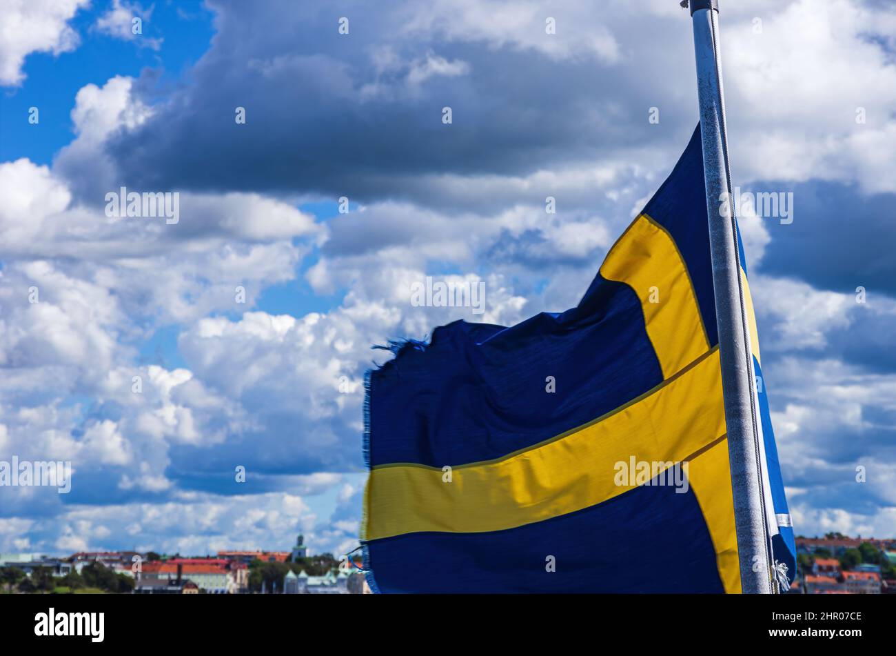 Die schwedische Flagge fliegt im Wind am Heck eines Schiffes vor dem Hintergrund der Küste. Stockfoto