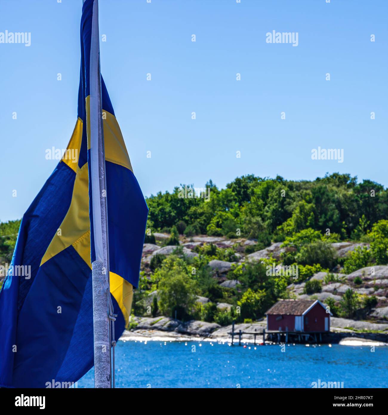 Die schwedische Flagge fliegt im Wind am Heck eines Schiffes vor dem Hintergrund der Küste. Stockfoto