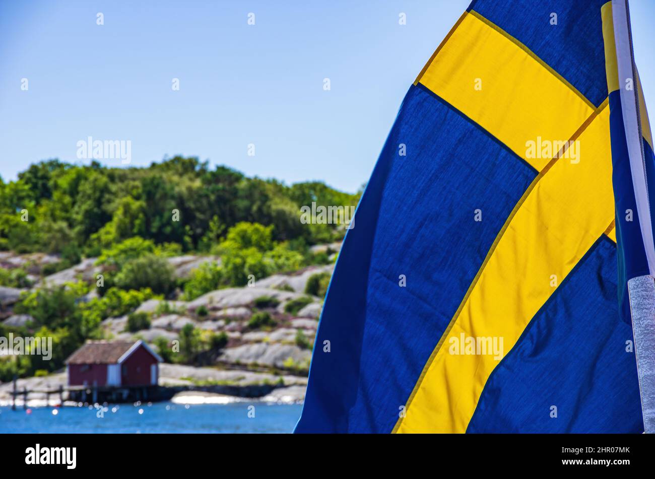 Die schwedische Flagge fliegt im Wind am Heck eines Schiffes vor dem Hintergrund der Küste. Stockfoto