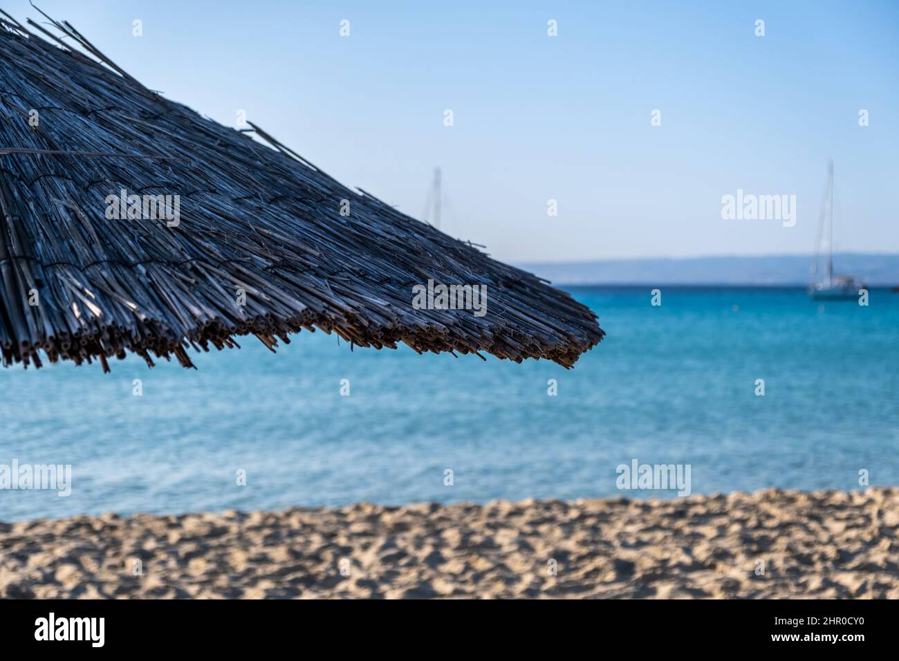 Strohschirm aus der Nähe, verschwommener leerer Sandstrand. Sonniger Tag auf See. Blauer Himmel und Meer, Sommerurlaub in Griechenland Stockfoto