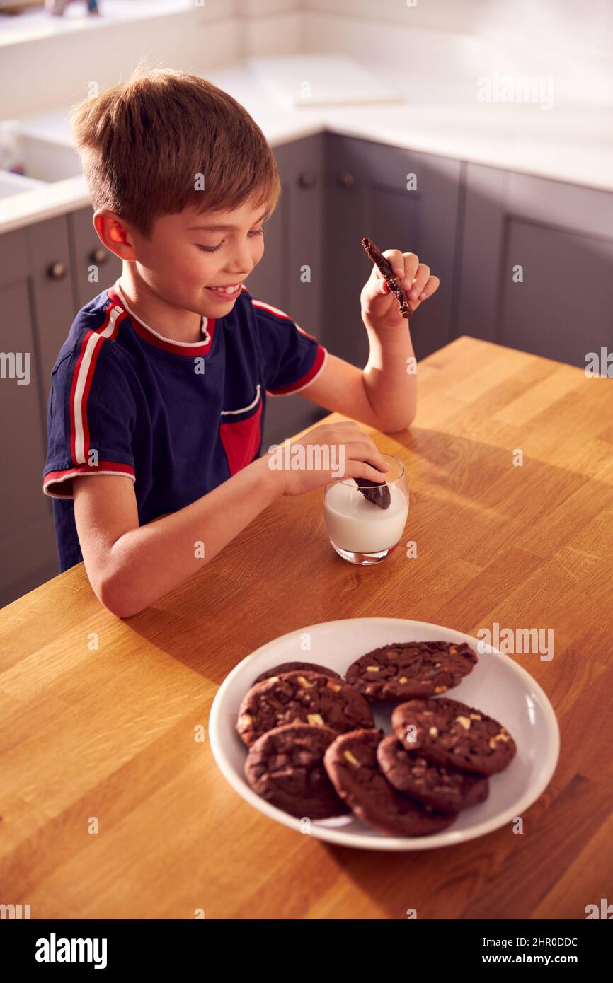 Junge Zu Hause Sitzt An Der Küchentisch Dunking Cookies In Glas Milch Stockfoto