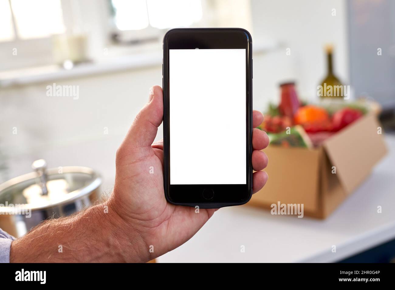 Hand In Der Küche Holding Telefon Mit Leerem Bildschirm Für Online-Mahlzeit Lebensmittel Rezept Kit Nach Hause Geliefert Stockfoto