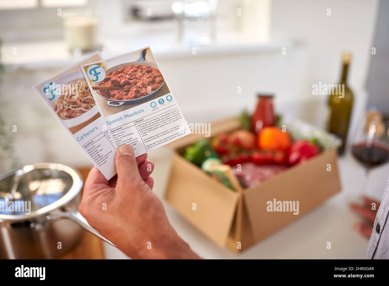 Nahaufnahme Der Hand In Der Küche Holding Rezepthekkarten Für Online-Mahlzeit Food Rezept Kit Nach Hause Geliefert Stockfoto