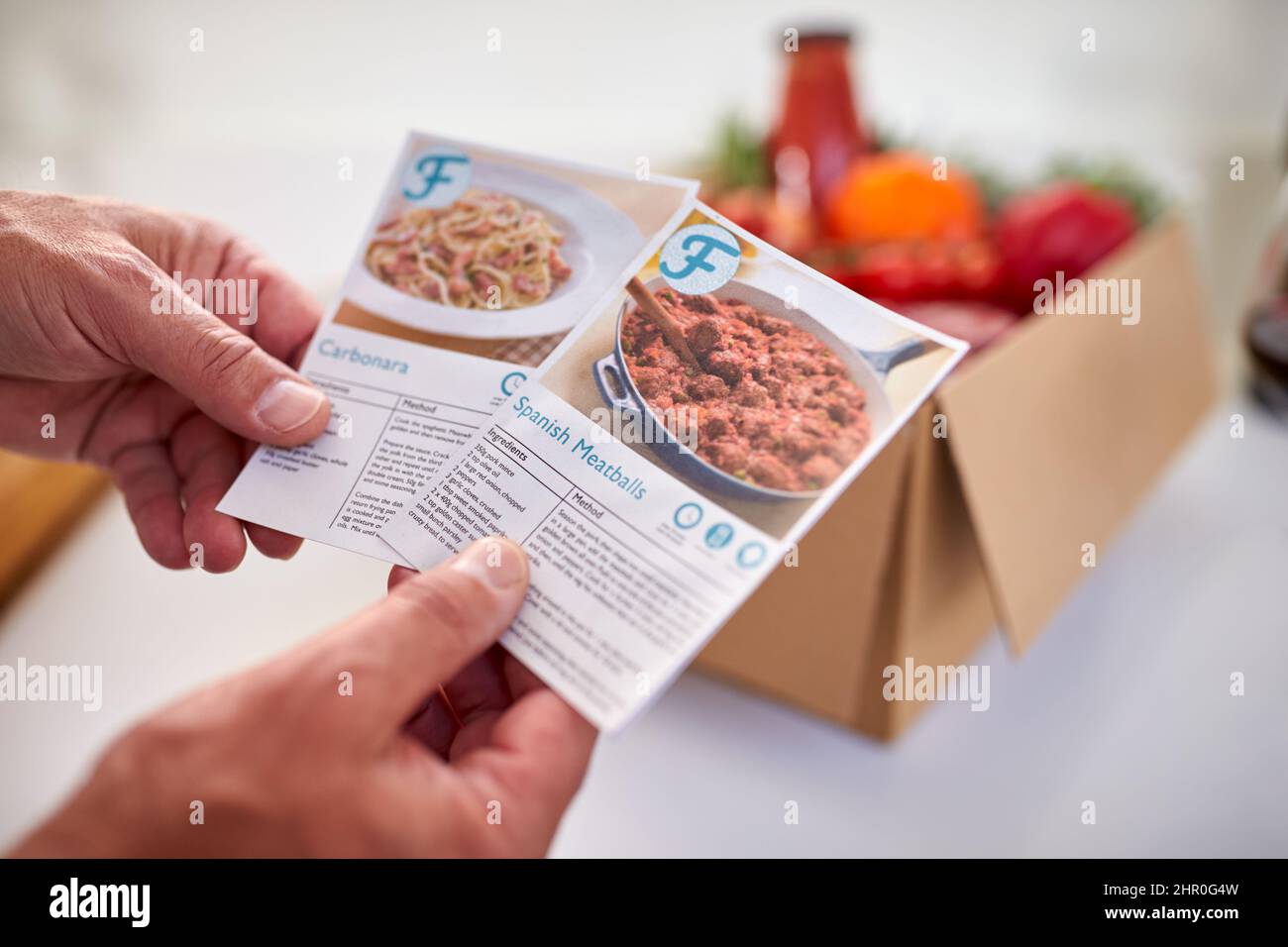 Nahaufnahme Der Hand In Der Küche Holding Rezepthekkarten Für Online-Mahlzeit Food Rezept Kit Nach Hause Geliefert Stockfoto