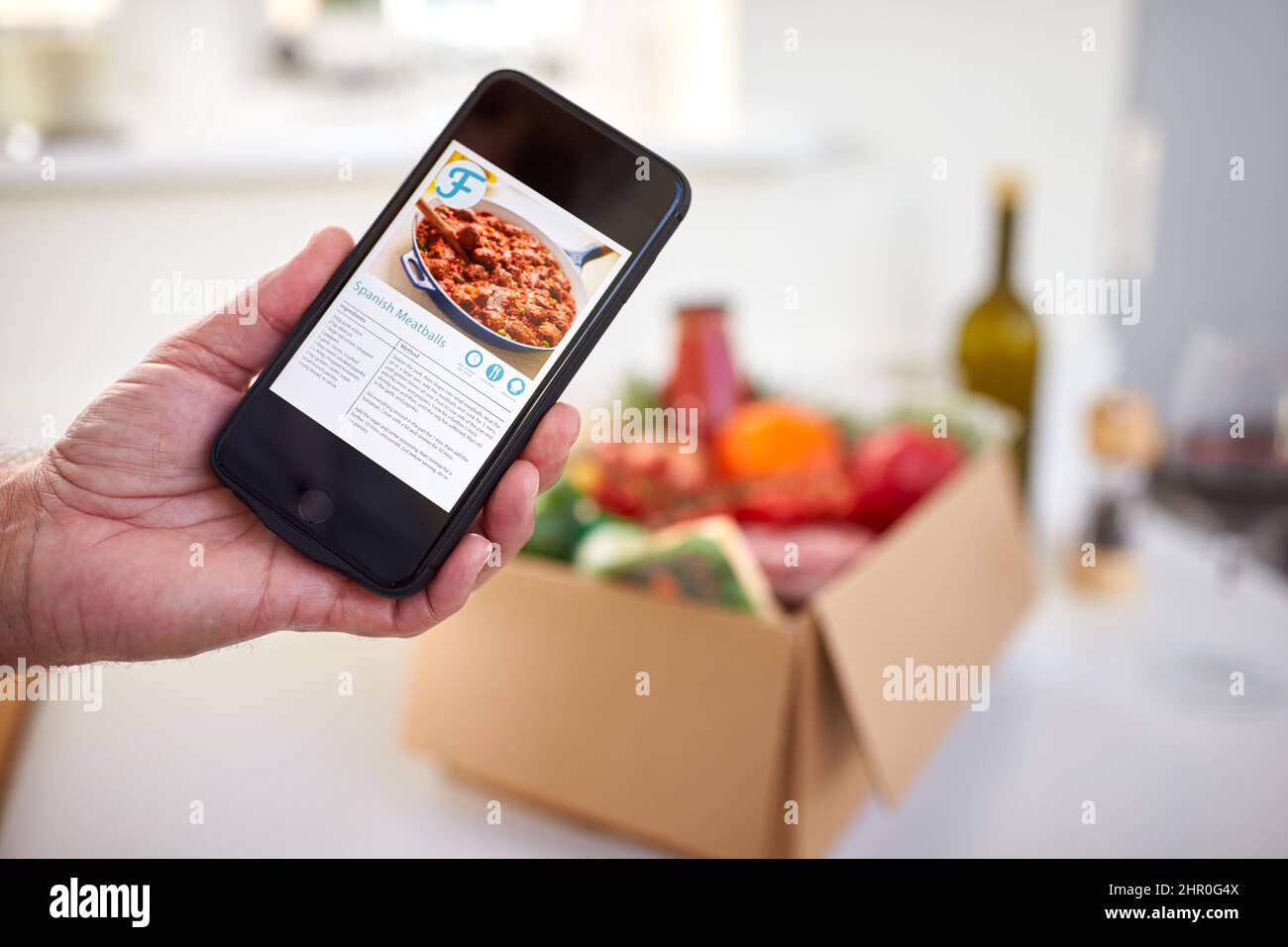 Hand In Der Küche Holding Telefon Mit Rezept Für Online-Mahlzeit Lebensmittel Rezept Kit Nach Hause Geliefert Stockfoto