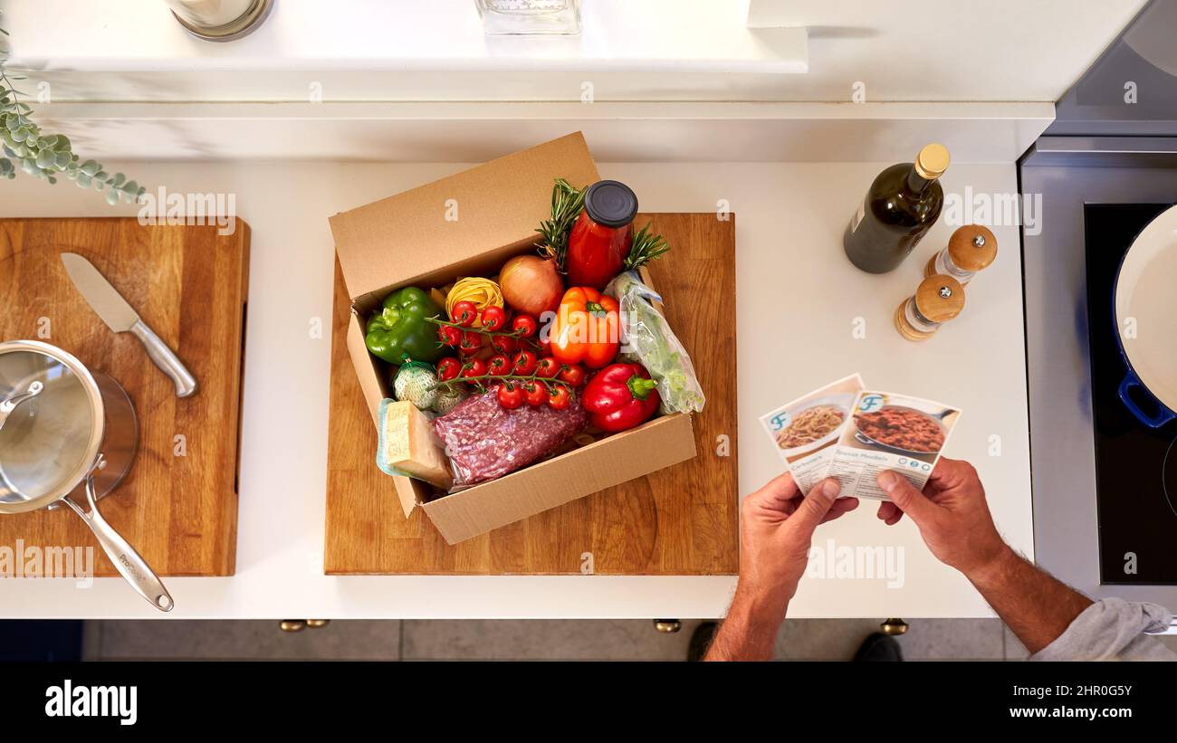Overhead Of Man In Kitchen Holding Rezept Karten Für Online-Mahlzeit Lebensmittel Rezept Kit Nach Hause Geliefert Stockfoto