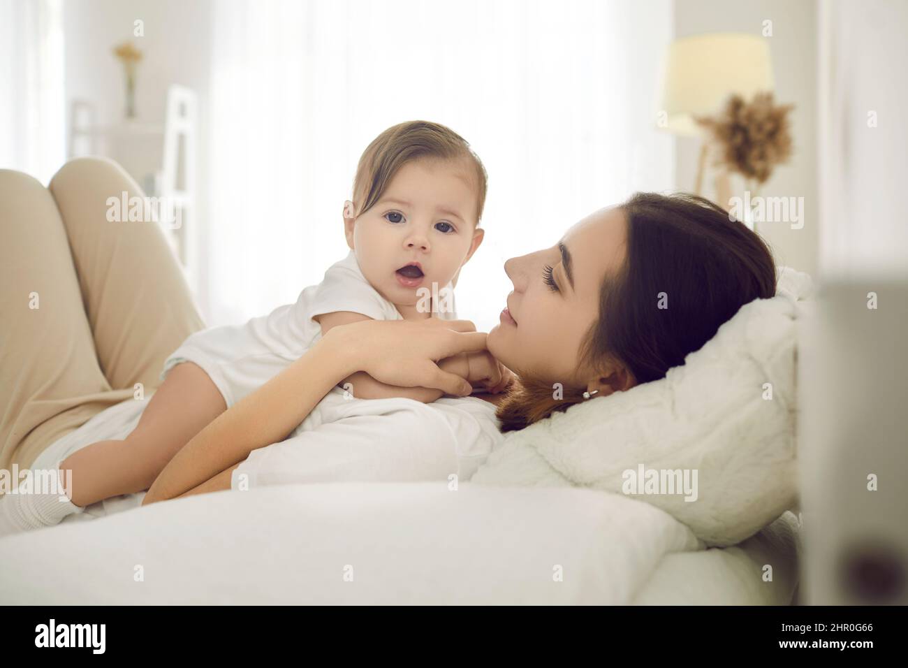 Glückliche junge Mutter zusammen mit ihrem süßen liebenswerten Baby kuscheln auf dem Bett zu Hause Stockfoto