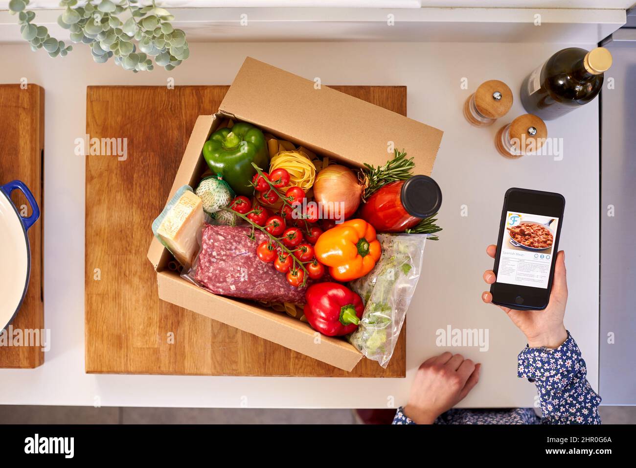 Hand In Küche Holding Telefon Mit Rezept Auf Dem Bildschirm Für Online-Lebensmittel-Rezept-Kit Nach Hause Geliefert Stockfoto