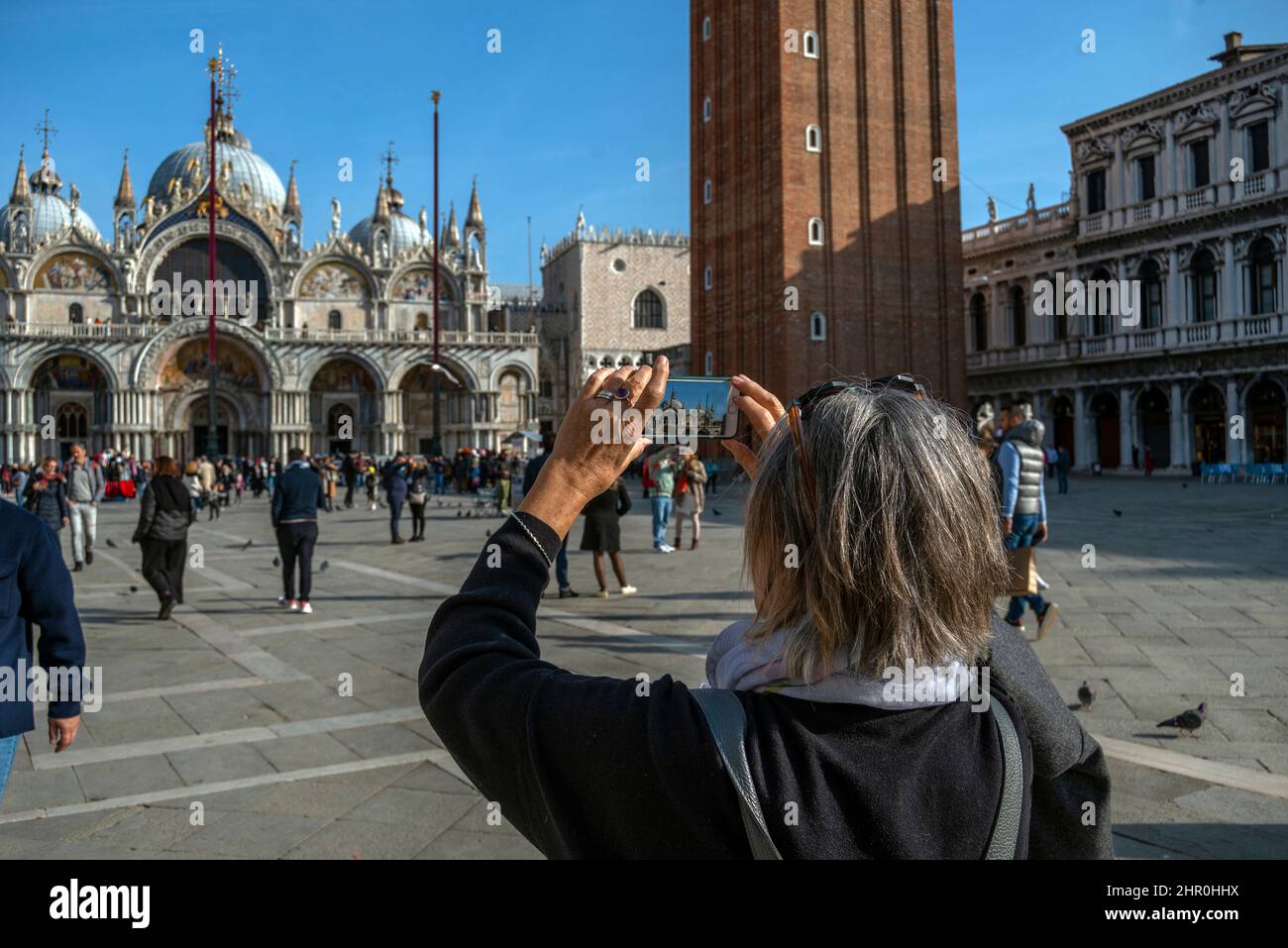 Eine Rückansicht einer Frau mit iPhone, die eine Aufnahme der Markusbasilika, des Markusplatz, von Venedig, Italien, gemacht hat. Stockfoto