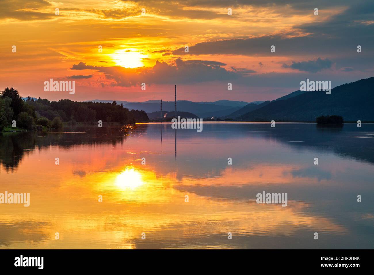 Industrielandschaft mit Schornsteinkonstruktionen, die sich bei Sonnenuntergang auf der Wasseroberfläche des Staudamms spiegeln. Zilina-Staudamm im Norden der Slowakei, Europa. Stockfoto