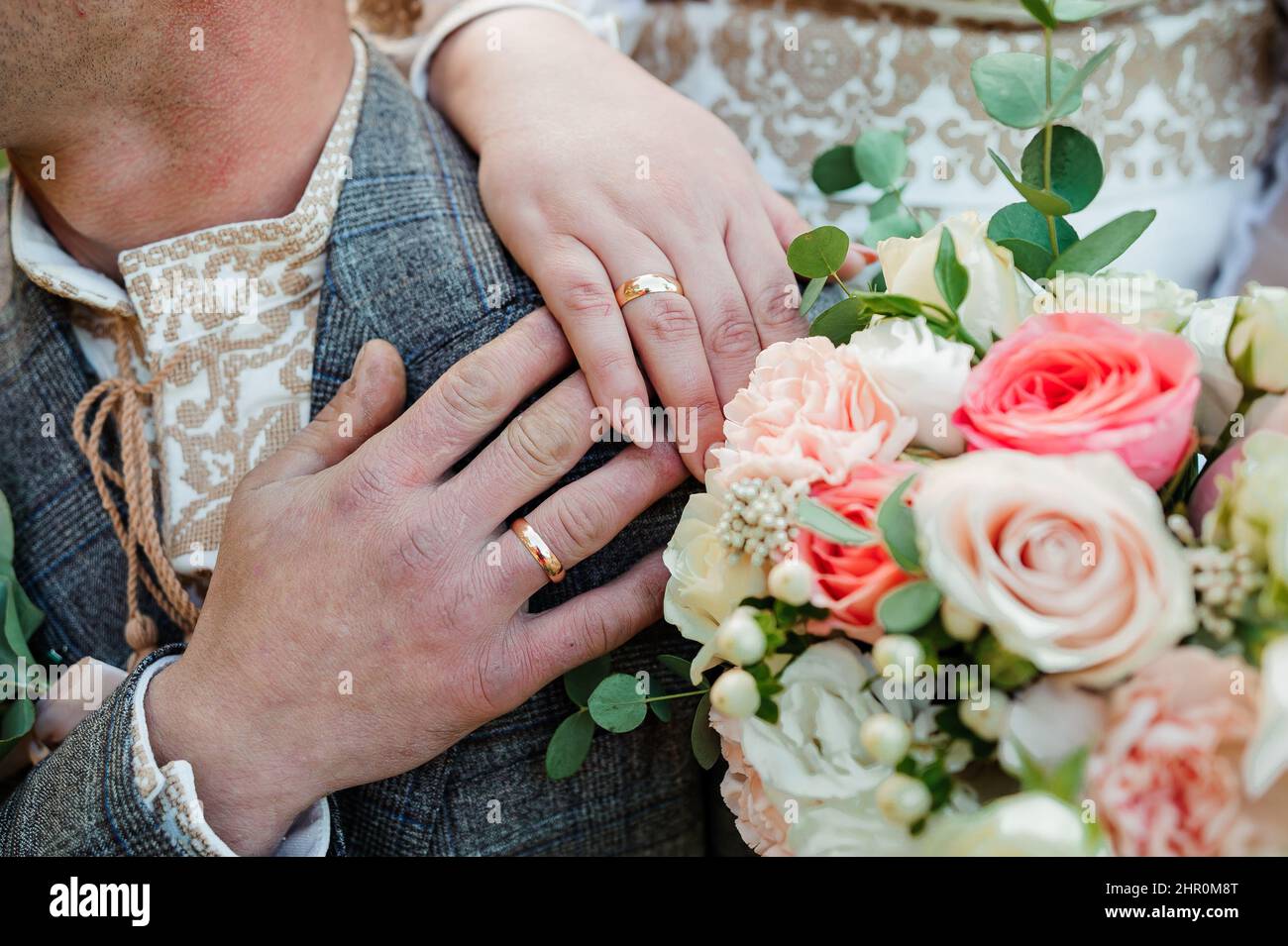 Goldene Eheringe, Hände der Braut und des Bräutigams auf einem Blumenstrauß Stockfoto