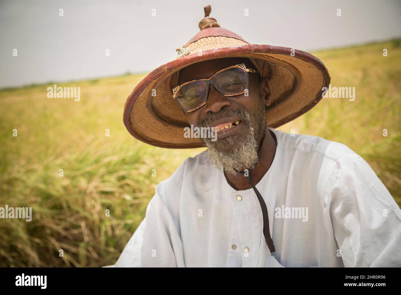 Ein Mann mit einem traditionellen Sonnenhut sitzt auf seinem Reisfeld im Senegal-Flussdelta im nördlichen Senegal in Westafrika. Stockfoto