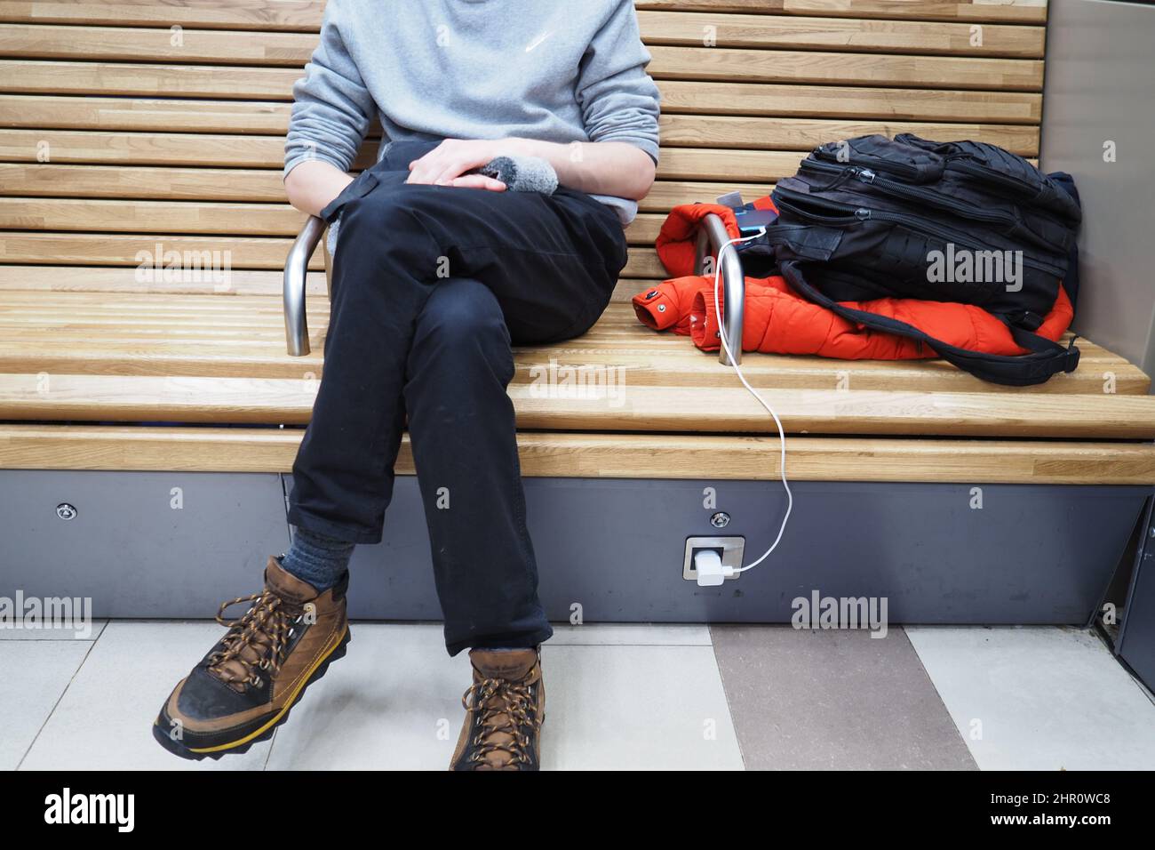 Ein junger Mann lädt im Wartezimmer des Bahnhofs ein Mobiltelefon. Hochwertige Fotos Stockfoto