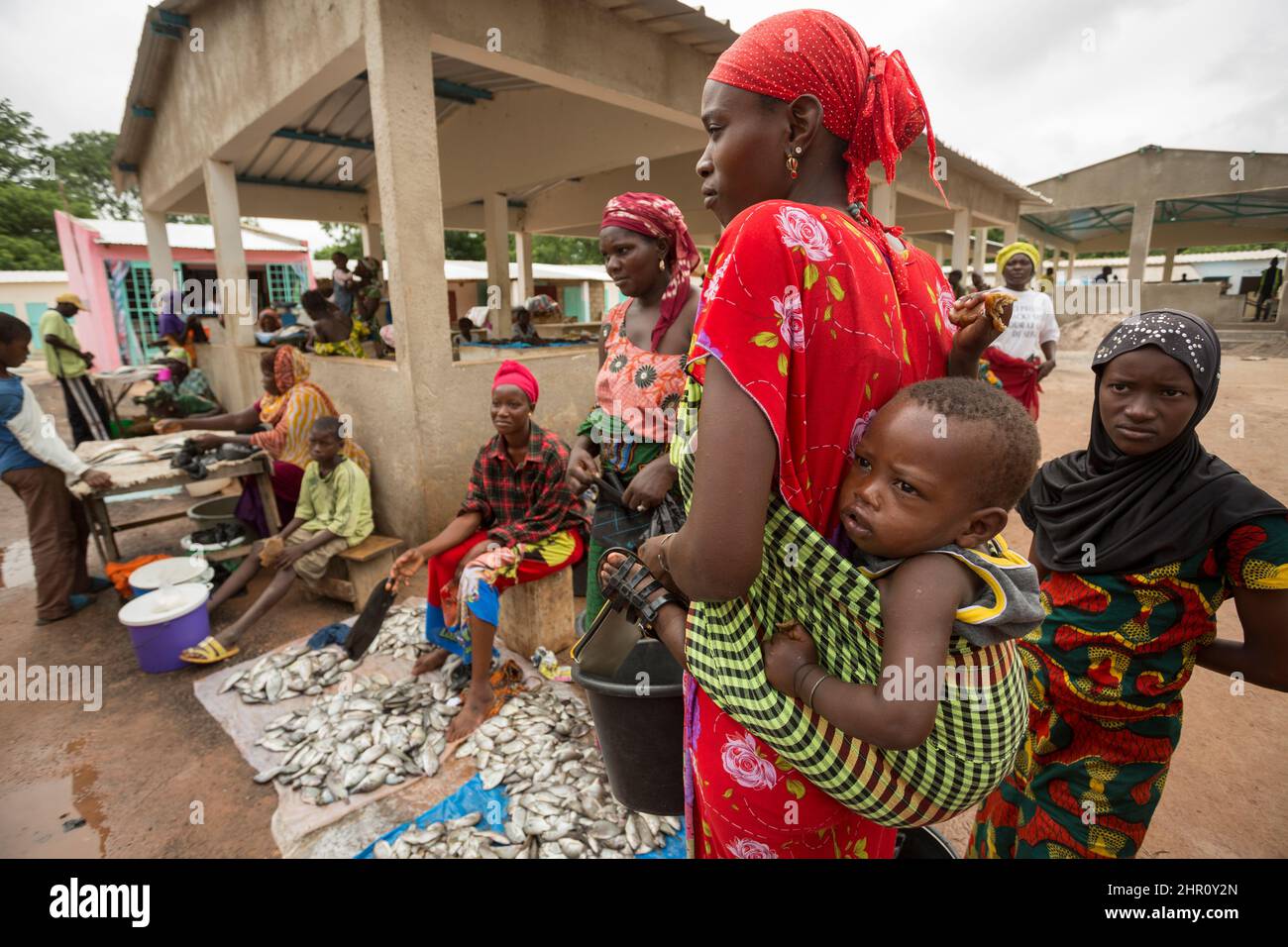 Eine Mutter trägt ihr Baby auf dem Rücken, während sie auf einem Markt in Tanaff, Senegal, Westafrika, frischen Fisch kauft. Stockfoto