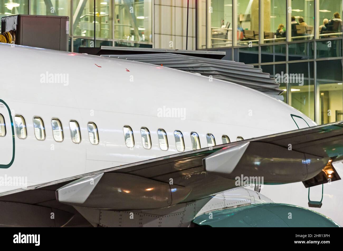 Blick auf den Rumpf eines Passagierflugzeugs mit Bullaugen im Hintergrund des Glasterminals des Flughafens in der Nacht Stockfoto