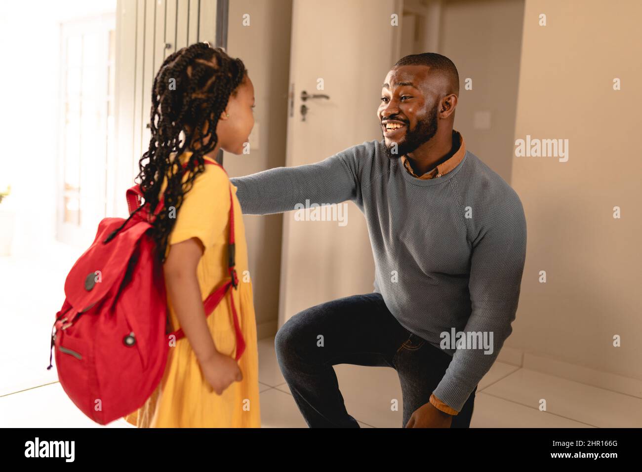 Ein glücklicher afroamerikanischer Mann kniete, während er mit seiner Tochter sprach, die am Hauseingang zur Schule ging Stockfoto