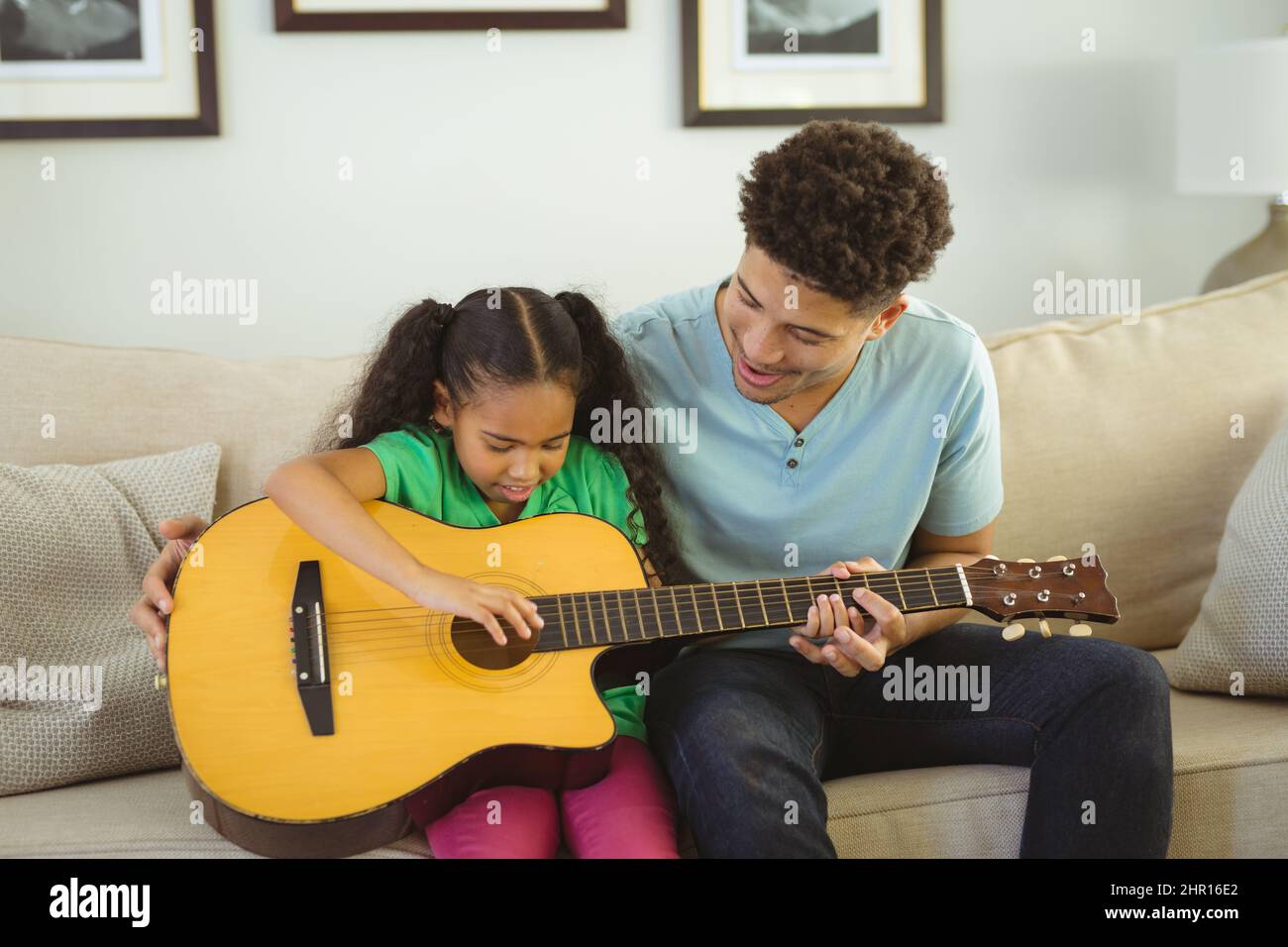 Glücklicher Biracial Vater lehrt Tochter Gitarre spielen, während zusammen auf dem Sofa im Wohnzimmer sitzen Stockfoto