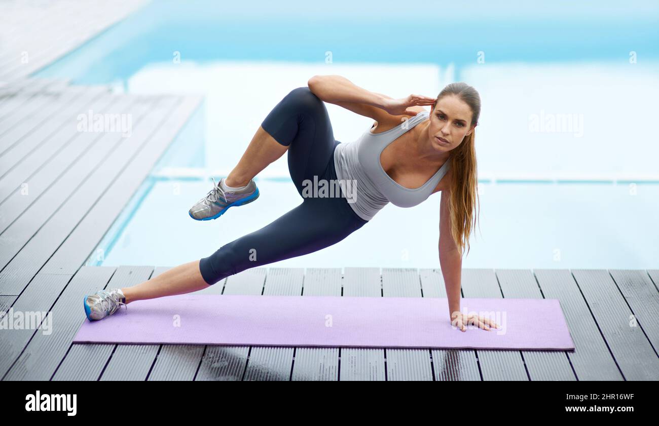 Stärke und Konzentration. Aufnahme einer wunderschönen jungen Frau, die im Freien neben einem Pool Yoga macht. Stockfoto
