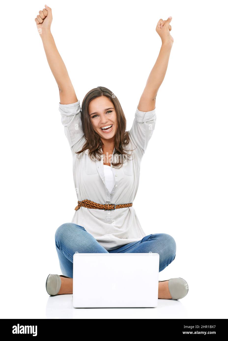 Tausend Treffer. Studioporträt einer jungen Frau, die vor einem Laptop sitzt und ihre Arme zur Feier angehoben hat. Stockfoto