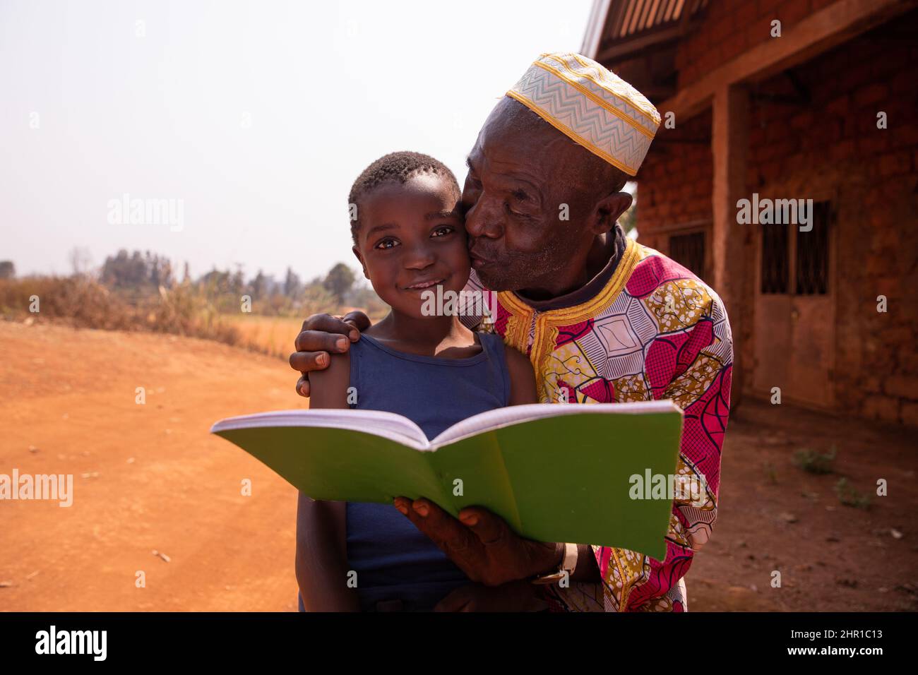 Afrikanischer Großvater küsst seinen Enkel, als sie zusammen ein Buch lesen. Liebe zwischen Großvater und Enkel Stockfoto
