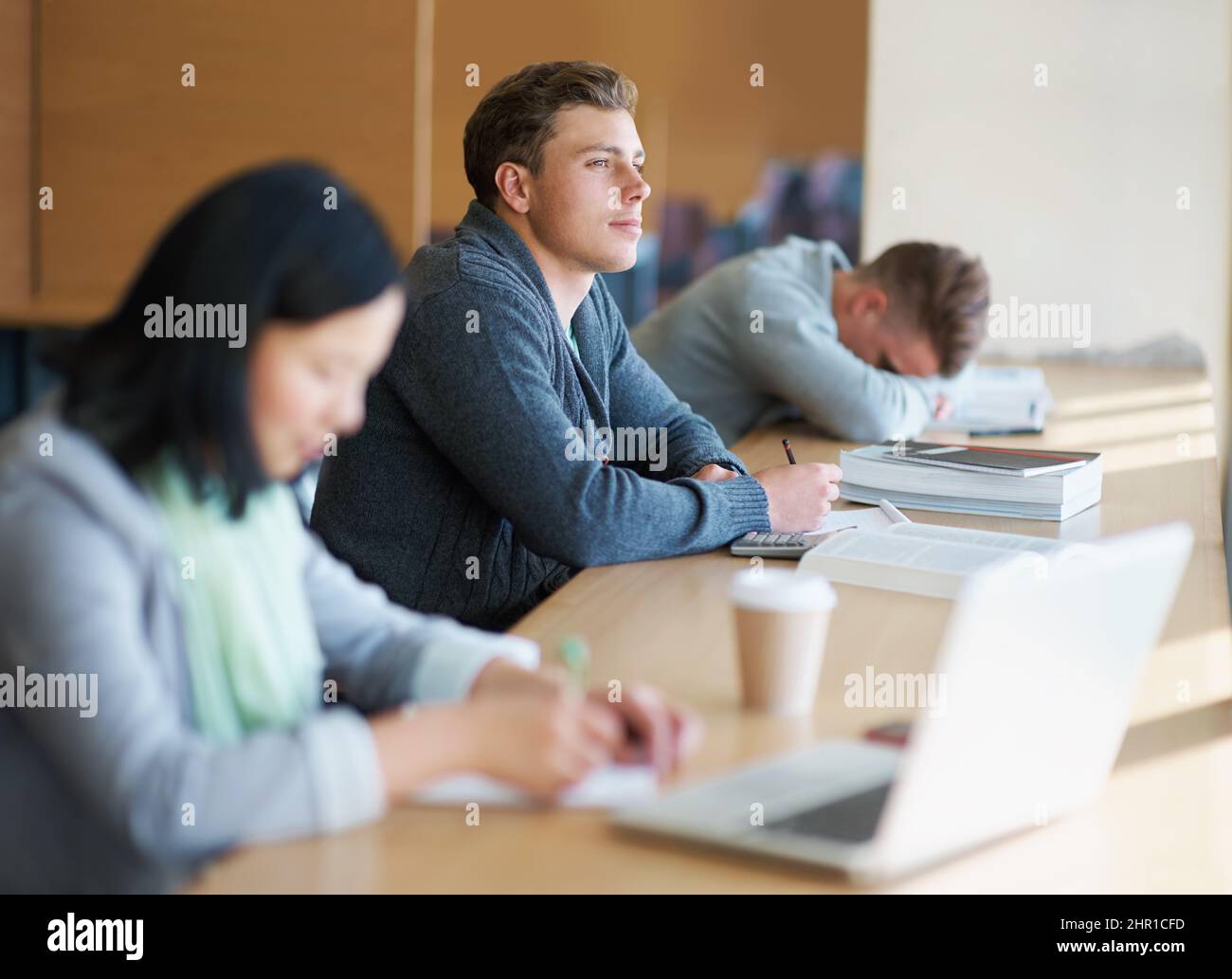 In letzter Minute ein paar Informationen zu sammeln. Ein junger Mann, der mit anderen Studenten die Bibliothek studiert. Stockfoto