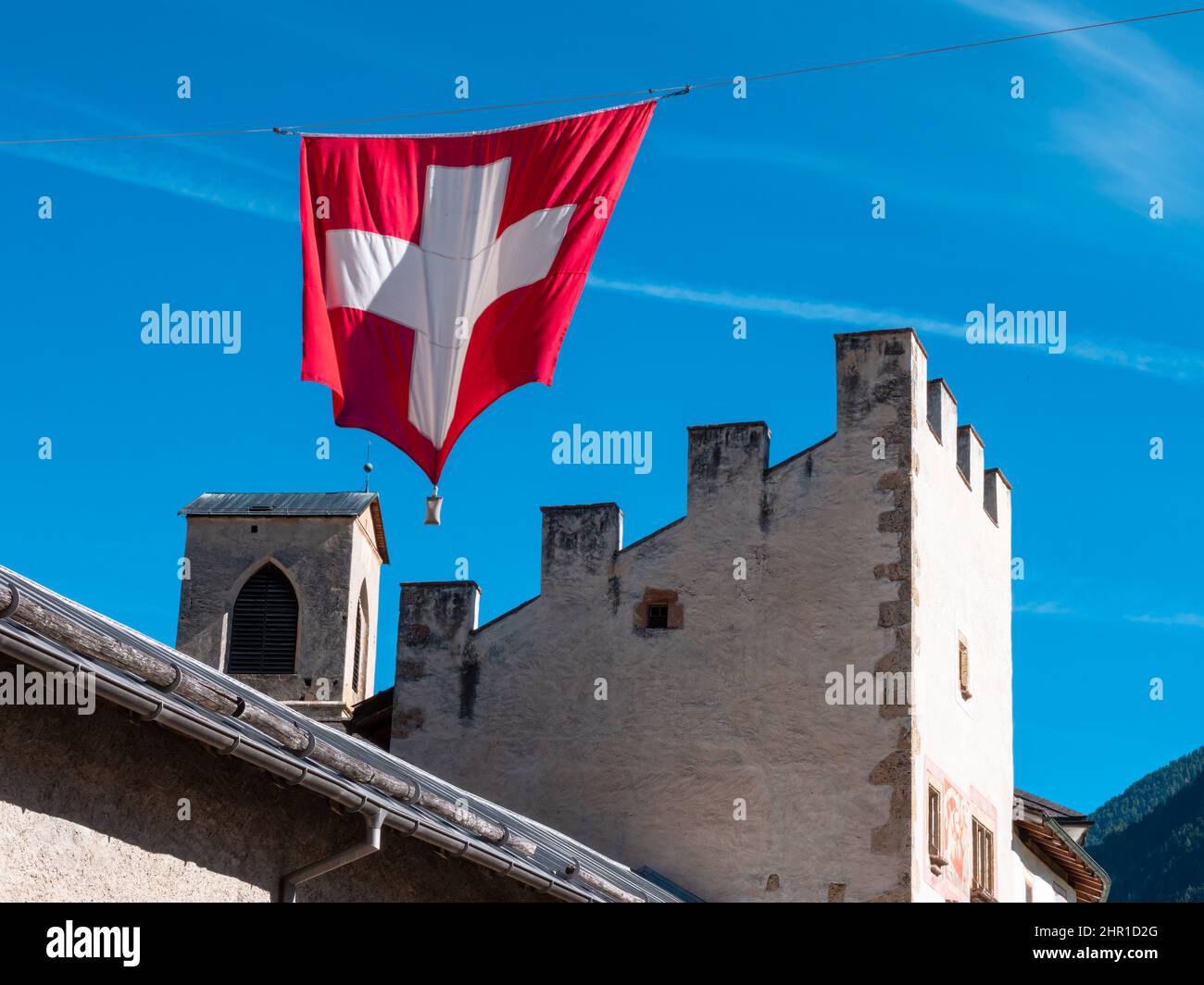 Mustair, Schweiz - 28. September 2021: Schweizer Nationalflagge über mittelalterlichen Mauern des schweizer Dorfes Mustair im Kanton Graubünden. Stockfoto