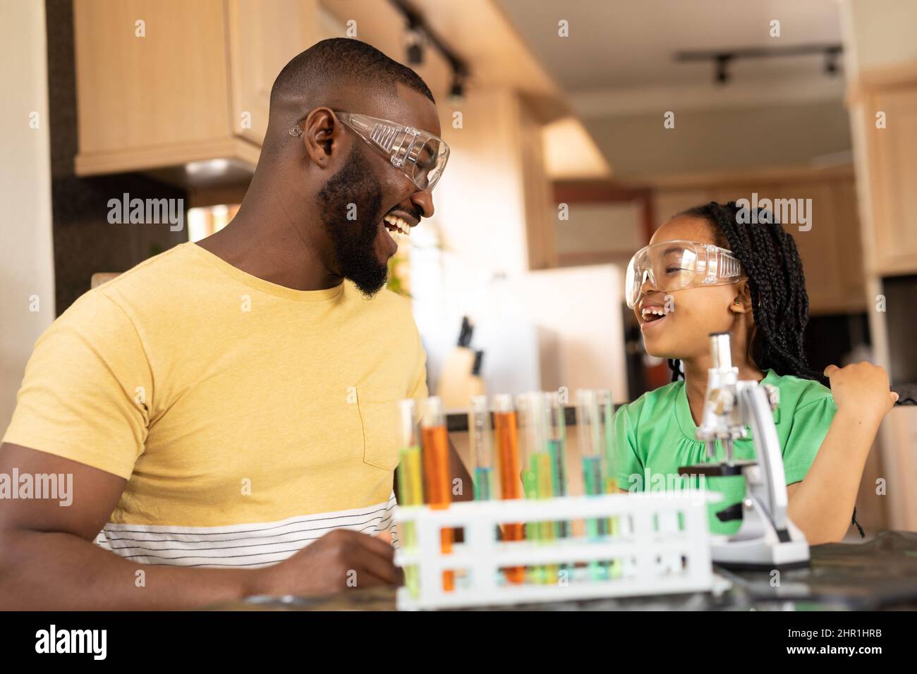 Fröhlicher afroamerikanischer Vater und Tochter, die zu Hause mit Reagenzglasgestell sitzen Stockfoto