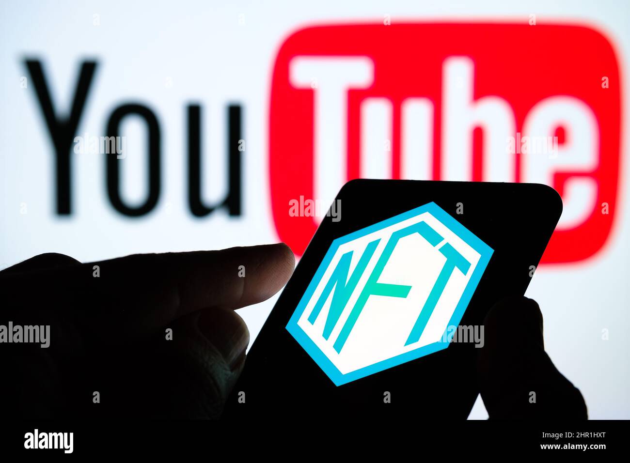NFT-Logo auf dem Bildschirm des Smartphones und verschwommenes YouTube-Logo auf dem Hintergrund. Selektiver Fokus. Stafford, Großbritannien, 24. Februar 2022 Stockfoto