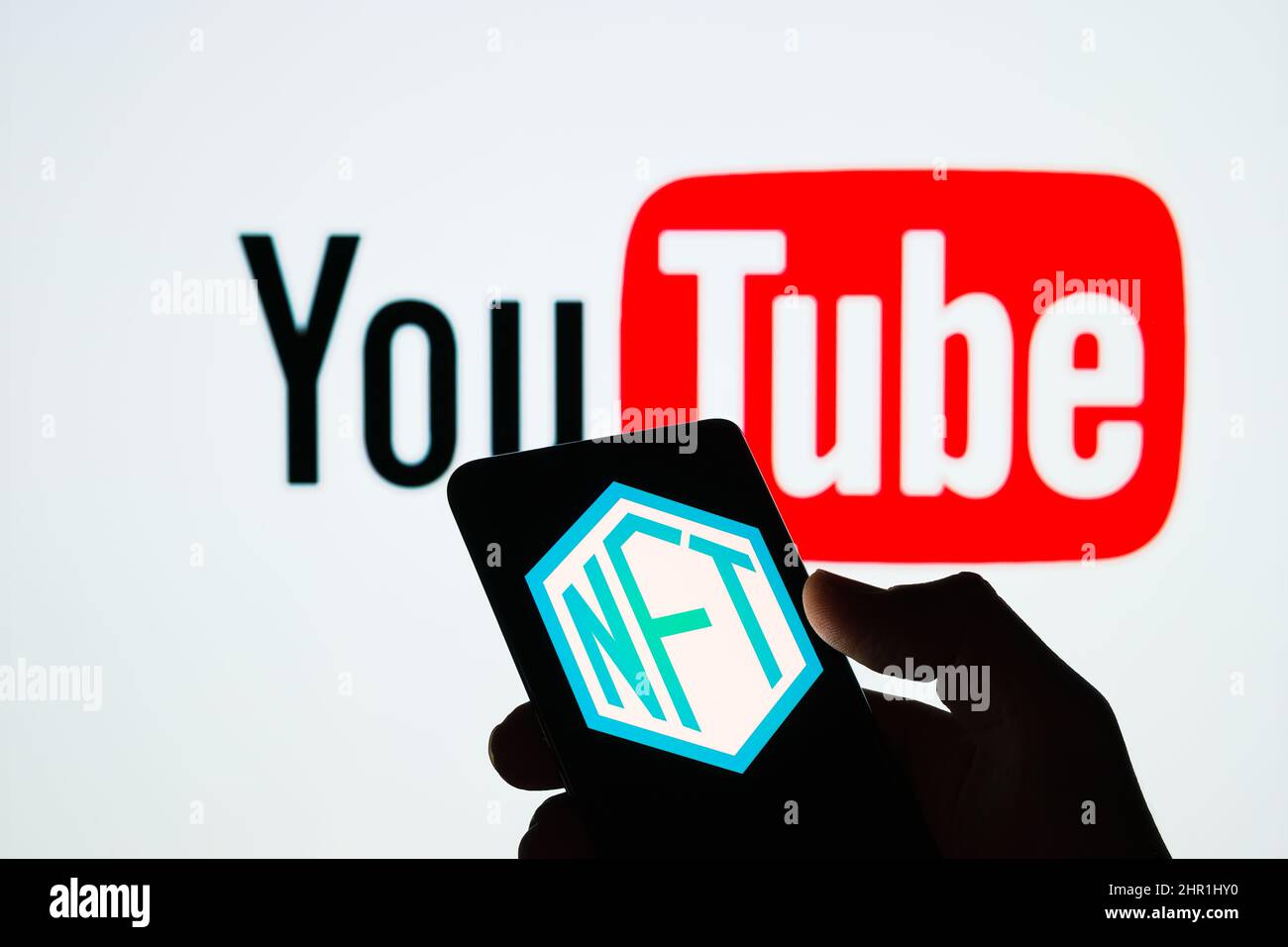 NFT-Logo auf dem Bildschirm des Smartphones und verschwommenes YouTube-Logo auf dem Hintergrund. Selektiver Fokus. Stafford, Großbritannien, 24. Februar 2022 Stockfoto