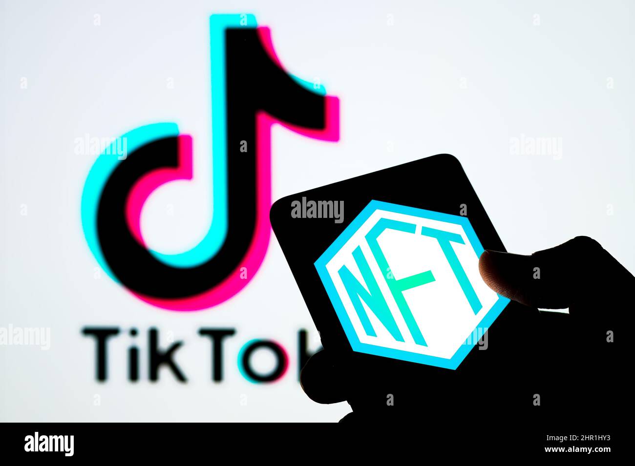 NFT-Logo auf dem Bildschirm des Smartphones und verschwommenes TikTok-Logo auf dem Hintergrund. Selektiver Fokus. Stafford, Großbritannien, 24. Februar 2022 Stockfoto