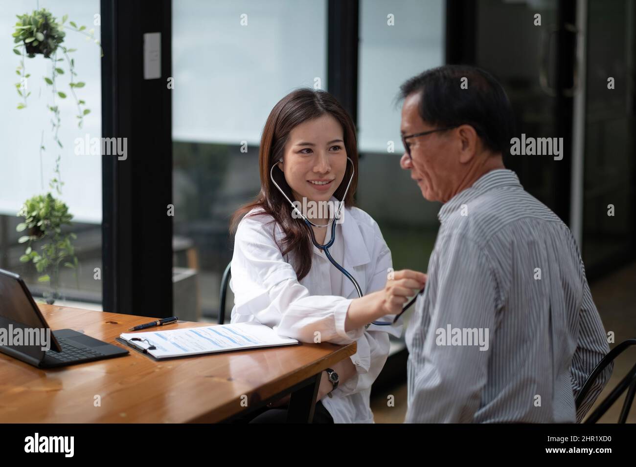 Stethoskop-Untersuchung. Attraktive fröhliche asiatische Ärztin, die älteren Menschen beim Stethoskop zuhört Stockfoto