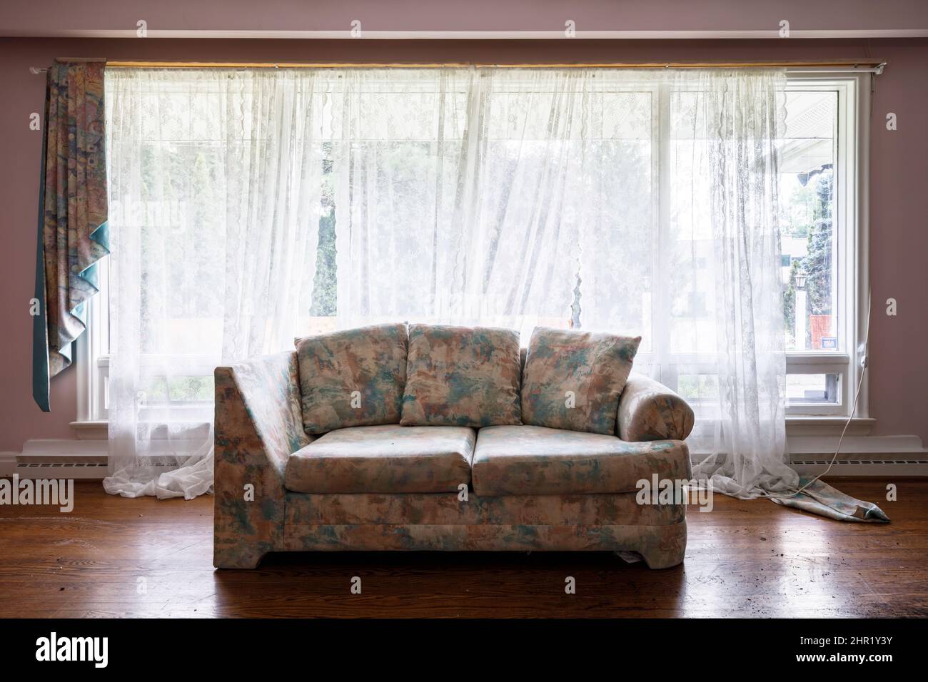 Eine hässliche Couch in einem ansonsten leeren Raum vor einem Fenster. Dieses Haus wurde abgerissen. Stockfoto